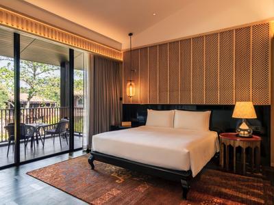 Modern hotel room with large bed, balcony, and green outdoor view.