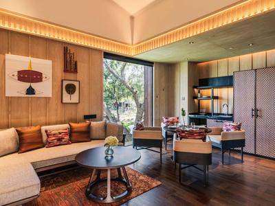 Modern hotel room with a sofa area, dining table, and large window overlooking greenery.