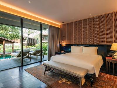 Modern hotel room with large bed and glass doors opening to garden with lounge chairs.