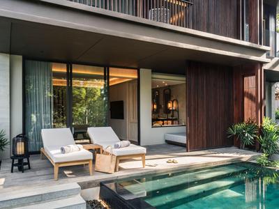 Modern hotel balcony with pool and two lounge chairs beside a glass-walled room.