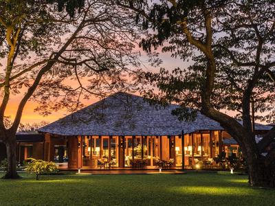 A modern hotel building with large windows at sunset, surrounded by trees and grass.