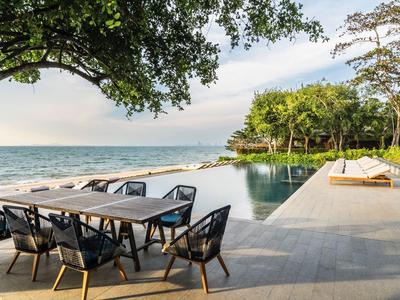 Modern outdoor area with dining table, pool, and ocean view at a tropical hotel.