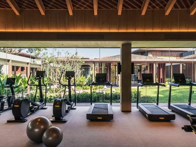 Gym with equipment overlooking a garden in a hotel complex.