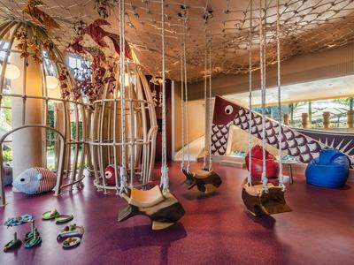 Hotel children's play area with swings, slides, and colorful safe flooring.