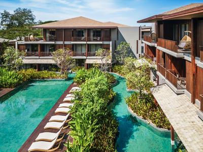 Modern hotel complex with pool and tropical garden area under blue sky.