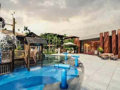Modern outdoor pool area with water features and wooden bar in a relaxed hotel setting.