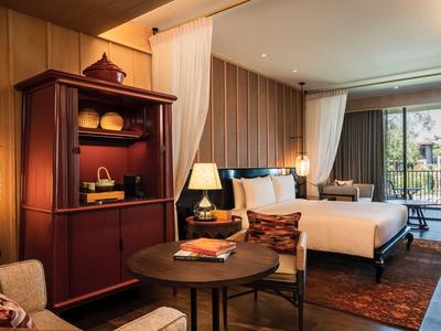 Bright hotel room with double bed, wooden furniture, and balcony overlooking greenery.