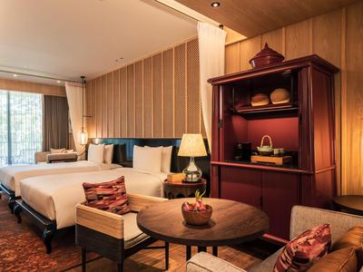 Modern hotel room with bed, armchair, table, and cabinet with shelves.