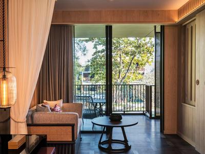 Modern hotel room with sofa and balcony overlooking trees.