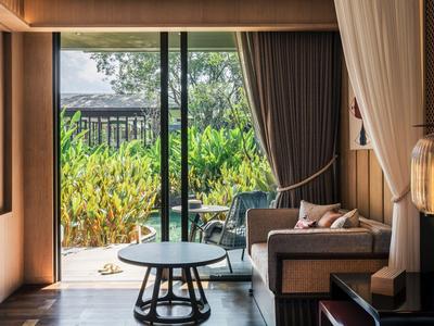 Cozy hotel room area with sofa, table, and garden view through large sliding glass door.