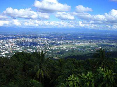 Vista da una collina boscosa su una vasta valle con città e cielo nuvoloso.
