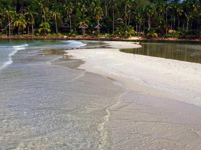 Spiaggia limpida con sabbia bianca e foresta tropicale sullo sfondo.