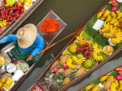 Three boats filled with tropical fruits, steered by a person wearing a straw hat, aerial view.