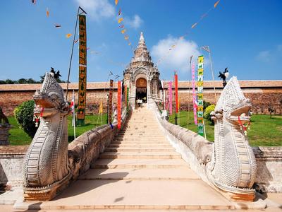 Temple stairs with dragon-shaped railings and colorful flags under clear sky.