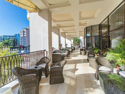 Großer Balkon mit Korbstühlen und Blick auf Stadtgebäude bei sonnigem Wetter.