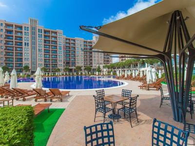 Großer Außenpool mit Sonnenliegen und Sonnenschirmen vor einem Hotelgebäude.