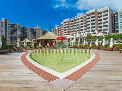 Herzförmiger Pool mit Liegestühlen und mehrstöckigem Hotel im Hintergrund bei sonnigem Himmel.