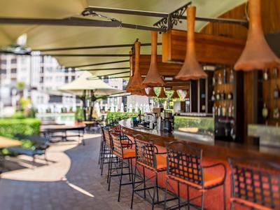 Moderner Barbereich im Freien mit Barhockern und Blick auf einen Pool in einer Hotelanlage.