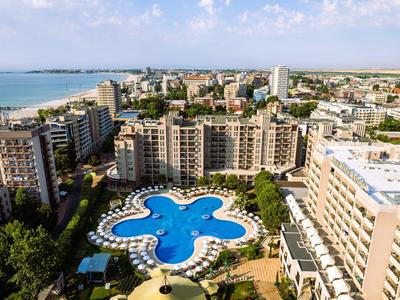 Blick auf ein Hotel mit einem großen, blauen Pool in der Form eines Kleeblatts und der Küste im Hintergrund.