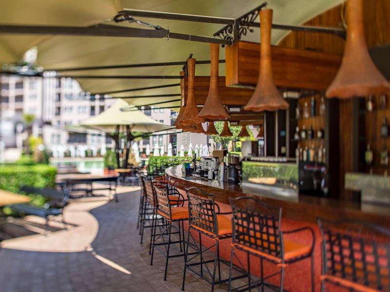 Offene Bar mit Hockern und Blick auf Außenbereich eines Hotels an einem sonnigen Tag