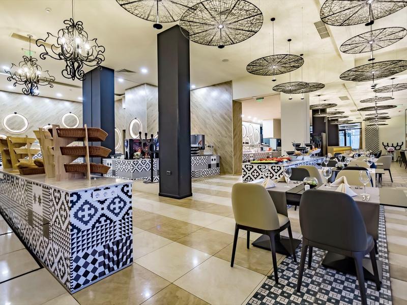 Helles, modernes Restaurant mit gemustertem Fliesenboden und grauen Stühlen an gedeckten Tischen.