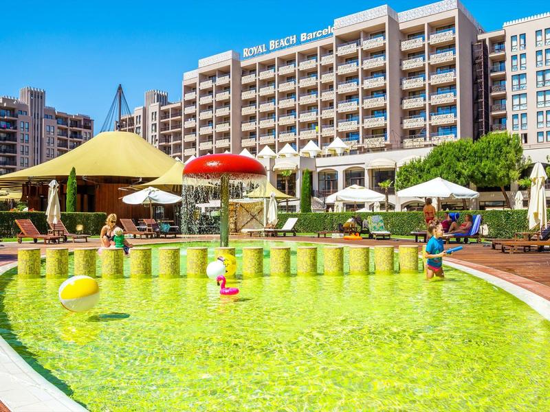 Außenpool mit Wasserspielplatz vor einem großen Hotelgebäude unter blauem Himmel