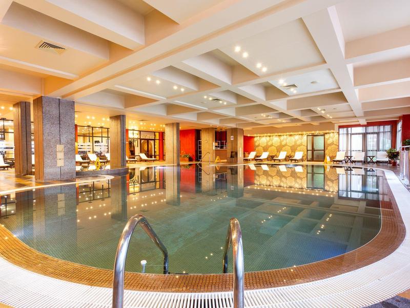 Großes, elegantes Hallenbad in einem Hotel mit weißer Decke und warmen Farbtönen.