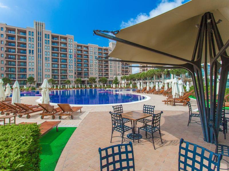 Großer Außenpool mit Sonnenliegen und Sonnenschirmen vor einem Hotelgebäude.