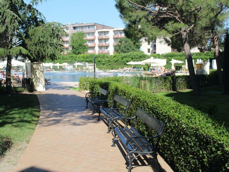 Gepflasterter Weg neben einem Pool mit Bänken und umgebenden Grünflächen in einem Hotelgarten