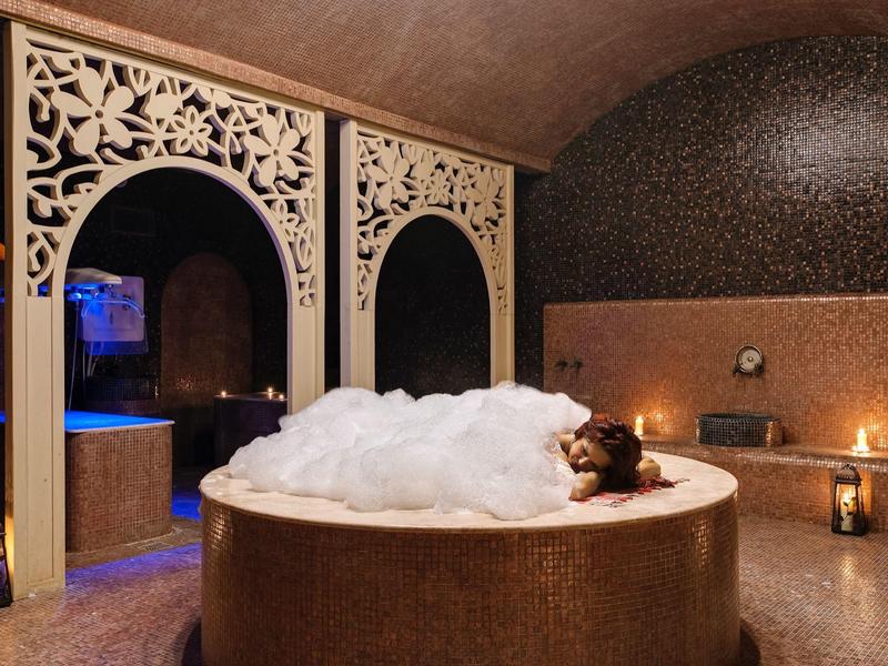 Runde Badewanne mit Schaum in einem luxuriösen Spa-Raum mit Laternen und verzierter Wand