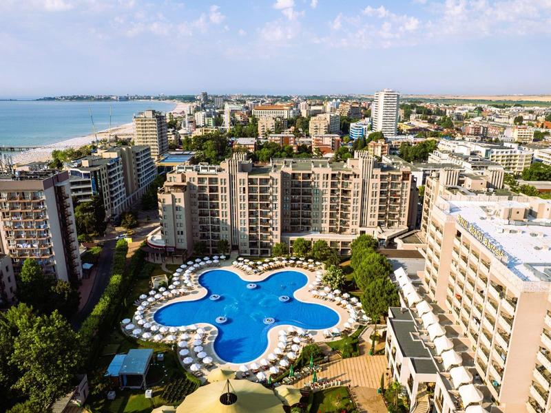 Blick auf ein Hotel mit einem großen, blauen Pool in der Form eines Kleeblatts und der Küste im Hintergrund.