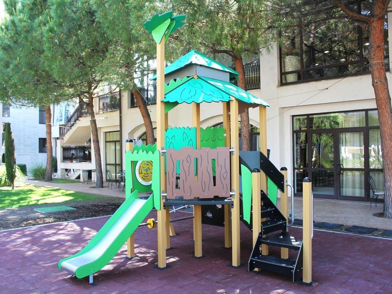Kinderspielplatz mit Rutsche und Klettergerüst neben einem Hotelgebäude und Bäumen
