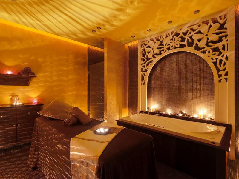 Beleuchteter Wellnessraum mit Massageliege, Kerzen und dekorativem Wandornament.