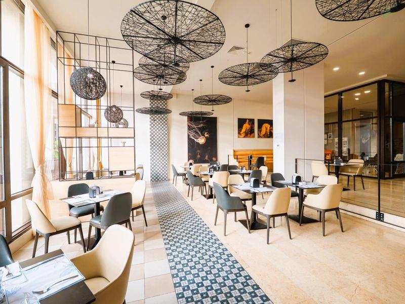 Helles Restaurant mit großen Fenstern, modernem Mobiliar und schwarzen Design-Lampen.