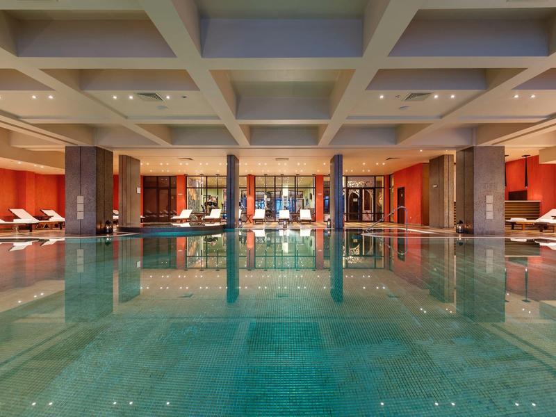 Moderner Innenpool mit ruhigem Wasser, umgeben von Liegestühlen und warmem Licht.