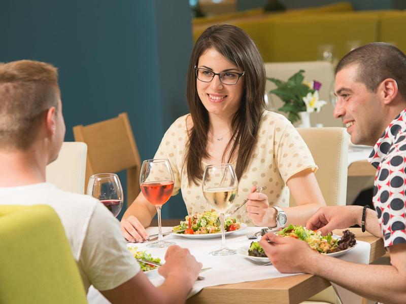 Tři lidé sedí v restauraci a společně si užívají jídlo.