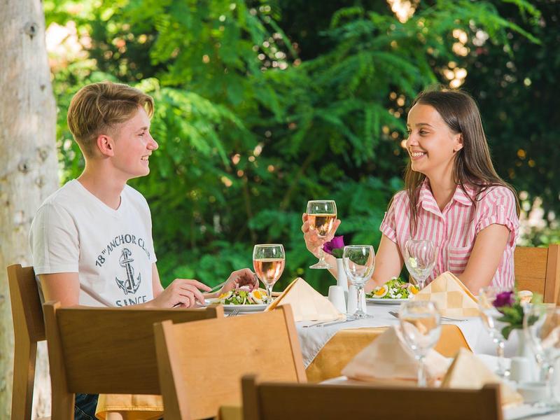 Pár si užívá jídlo a víno v zeleném venkovním prostoru hotelu.