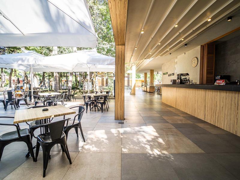 Světlá hotelová lobby s posezením a velkými okny otevírajícími se na terasu s slunečníky.