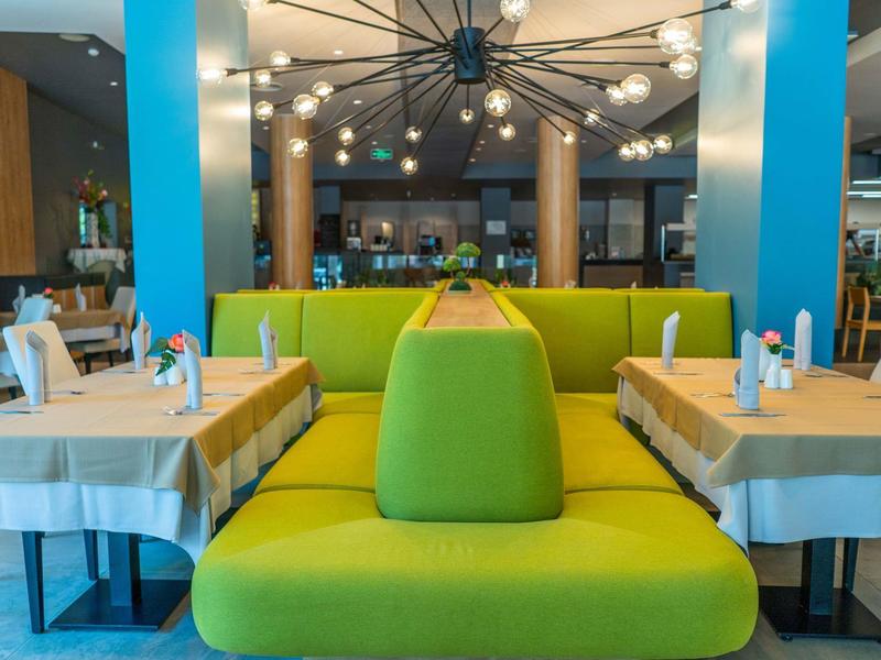 Moderní restaurace se zelenou lavicí a prostřenými stoly v světlé atmosféře