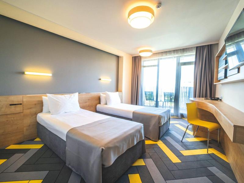 Moderní hotelový pokoj se dvěma jednolůžky, psacím stolem a balkonem se skleněnými dveřmi.