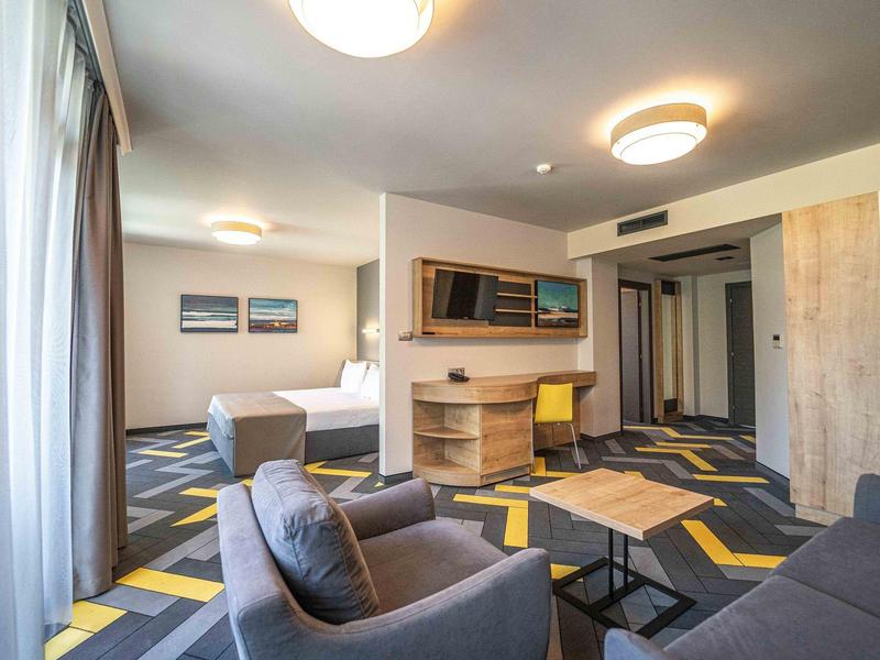 Moderně zařízený hotelový pokoj s postelí, pracovním stolem a posezením v teplých tónech.