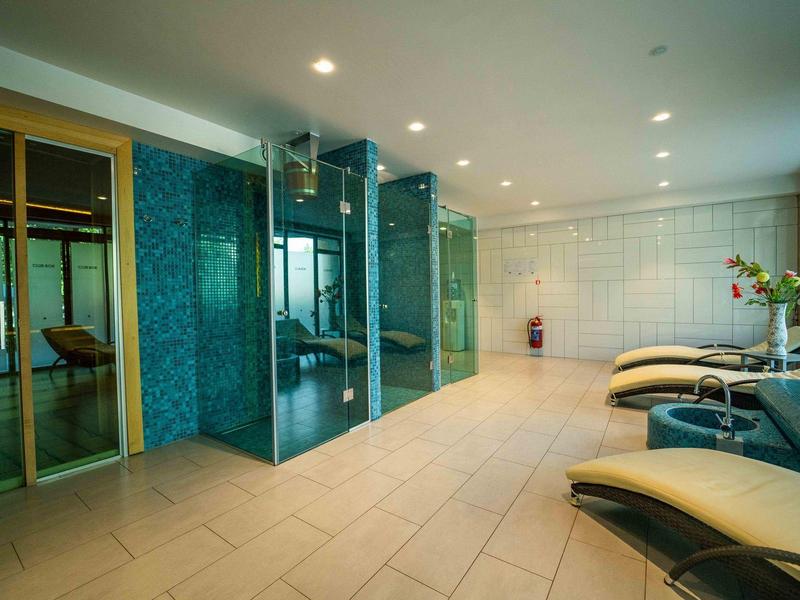 Moderní wellness prostor s parní sprchou, lehátky a velkými okny.