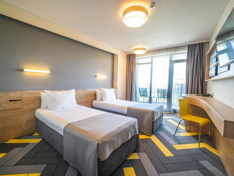 Moderně zařízený hotelový pokoj se dvěma jednolůžky, pracovním stolem a balkonem