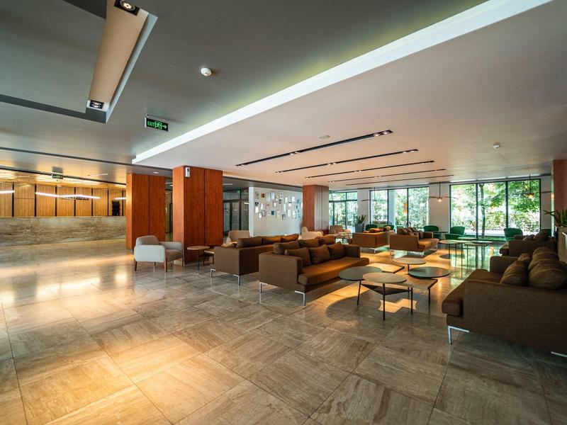 Prostorná hotelová lobby s velkými okny, elegantními sezeními a jasným osvětlením.