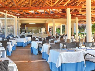 Großer, offener Restaurantbereich mit gedeckten Tischen und Holzdach bei Tageslicht.
