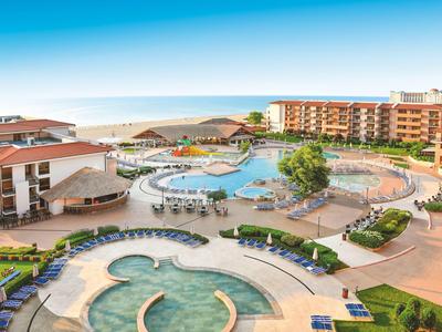 Hotelanlage mit mehreren Pools, Liegestühlen und mehrstöckigen Gebäuden am Meer unter blauem Himmel.