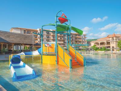 Wasserpark mit Rutsche, Klettergerüst und kleinem Pool unter blauem Himmel bei Sonnenschein.