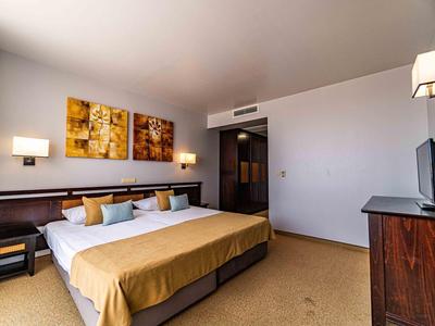 Ein modernes Hotelzimmer mit großem Doppelbett, zwei bunten Bildern an der Wand und Fernseher auf Kommode.