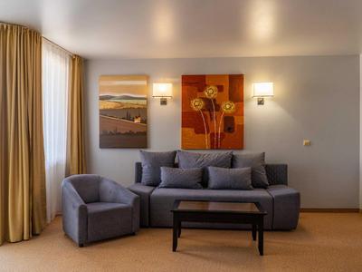Wohnzimmer mit grauem Sofa, Sessel, Holztisch, zwei Wandbildern und gelben Vorhängen.