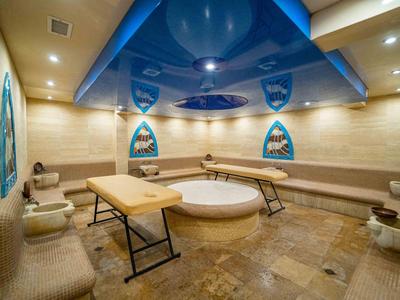 Großer Wellnessraum mit massagetischen, runden Whirlpool und gelblichem Marmorfußboden.